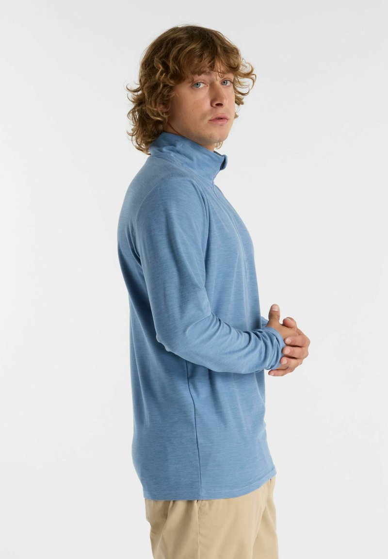 Chemise bleu clair à manches longues avec col montant, fabriquée en tissu doux. Le design présente une coupe droite et aucun motif ni accent visible.