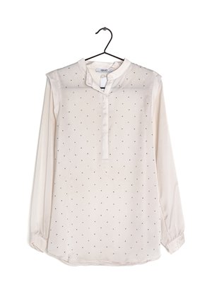 Vaaleanbeige pitkähihaisessa paidassa on mandariinikaulus, jossa on pieniä mustia pilkkuja koko paidan alueella ja napitus edessä.