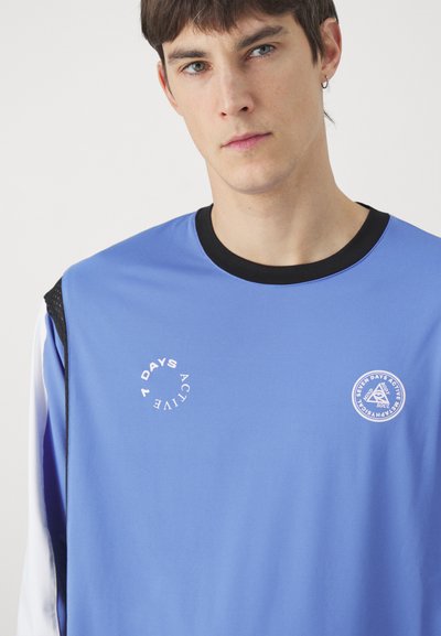 Blue athletic long-sleeve shirt with black collar. Features white printed logos on front, mesh accents on sleeves, and a sporty fit.