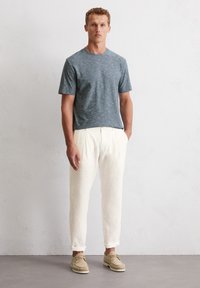 Helles blaue, strukturierte T-Shirt, weiße Leinenhose, hellbraune Schuhe. Einfaches Design, lockere Passform. Neutrale Farben mit minimalen Akzenten.