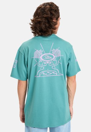 Camiseta de algodón verde menta con un diseño gráfico rosa en la parte de atrás, que representa manos y formas abstractas, con mangas cortas y un corte relajado.