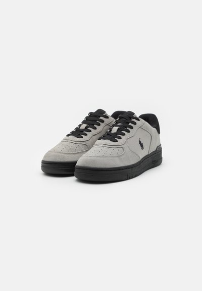 Gray suede sneakers with black accents, featuring perforated detailing, black laces, and a textured rubber sole. Logo present on the side.