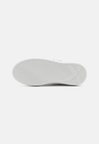 Hvit sneaker såle med bølgete mønster og en stor "K" form nær hælen, satt mot en enkel hvit bakgrunn.
