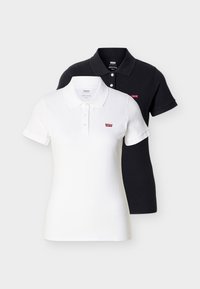 Δύο polo πουκάμισα Levi's με κοντό μανίκι, ένα λευκό και ένα μαύρο, καθένα με γιακά, τρία κουμπιά και ένα μικρό κόκκινο λογότυπο στο στήθος.