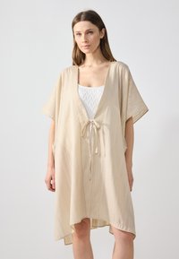 Beige kimono-tyylinen peittovaatetus, jossa on nauhakiinnitys, lyhyet hihat ja virtaava, tekstuuri kangas, jossa on hienovaraiset pystysuorat raidat.