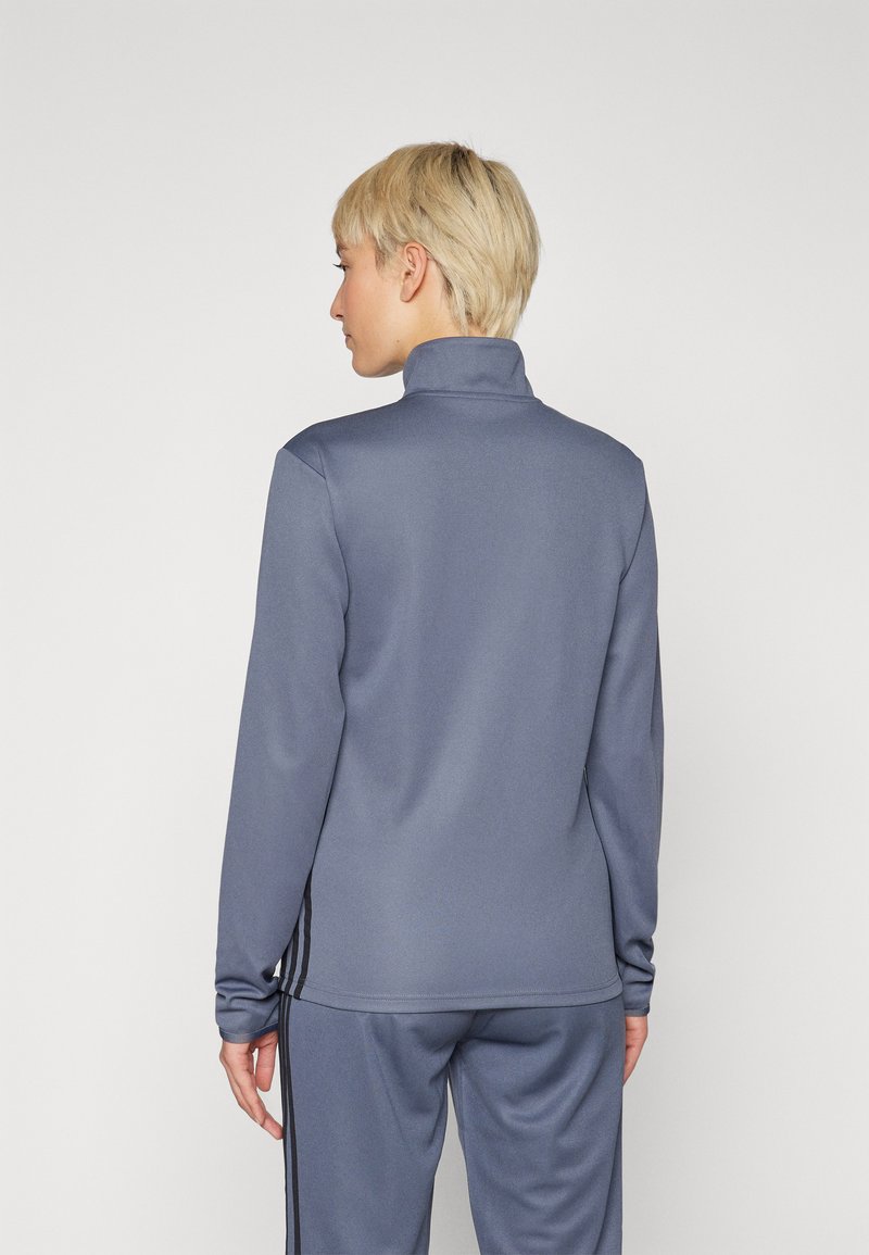 Graue sportliche Zip-Jacke mit hohem Kragen. Mit langen Ärmeln und schwarzen Streifen an den Seiten. Glattes, dehnbares Material.