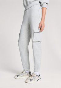 Jasnoszare dresy z elastycznym pasem, bocznymi kieszeniami oraz dwoma kieszeniami w stylu cargo. W zestawie z beżowymi i szarymi sneakersami.