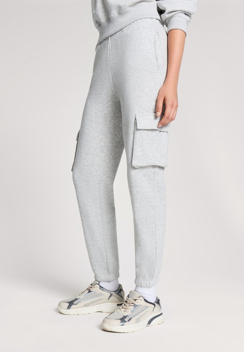 Jasnoszare dresy z elastycznym pasem, bocznymi kieszeniami oraz dwoma kieszeniami w stylu cargo. W zestawie z beżowymi i szarymi sneakersami.