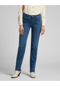 Jeans in denim blu con una vestibilità slim, design a cinque tasche e vita media, abbinati a mule con tacco color crema.