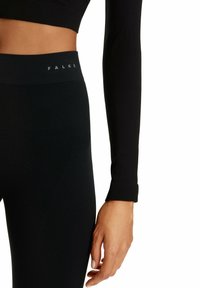 Schwarze Leggings mit geripptem Textur und Logo-Bund. Begleitet von einem eng anliegenden Langarmshirt mit einem Detail an den Bündchen.
