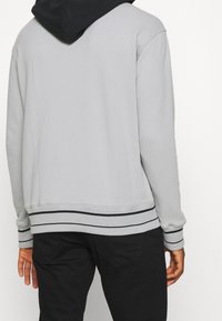 Sudadera gris con capucha negra, con puños y bajo acanalados con rayas negras, hecha de una tela suave y de textura lisa.