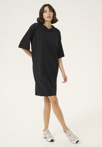 Svart, oversized t-shirt-klänning med korta ärmar, mjukt och slätt tyg, knälång, med rund halsringning och avslappnad silhuett.