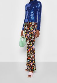 Camisa de botones azul con lentejuelas, pantalones acampanados de patrón floral, bolso verde menta y sandalias de dedo rosas.