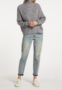 Grijze gebreide coltrui met een textuurpatroon, gecombineerd met lichtblauwe verwerkte jeans en witte sneakers.