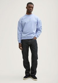 Lyseblå sweatshirt lavet af blødt stof, med rund udskæring og ribbede manchetter, sat sammen med mørke denimjeans og sorte sneakers.