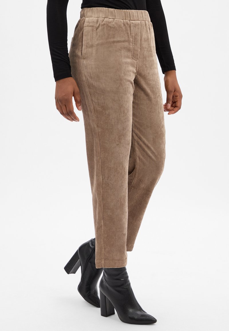 Brązowe spodnie typu corduroy o prostym kroju, z płaskim pasem, bocznymi kieszeniami i subtelną fakturą, zestawione z czarnymi botkami na obcasie.