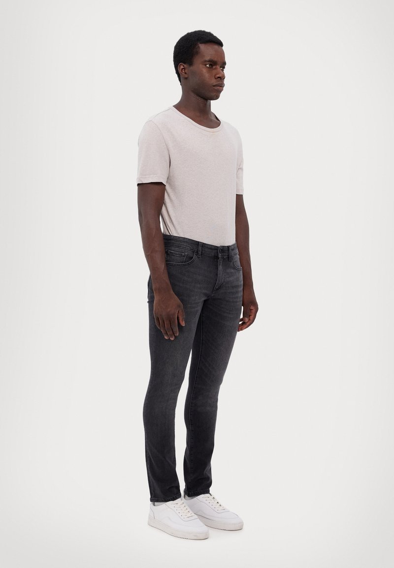 T-shirt en coton gris, coupe ajustée, associé à un jean en denim foncé et des baskets blanches. Design simple sans motifs ni accents remarquables.