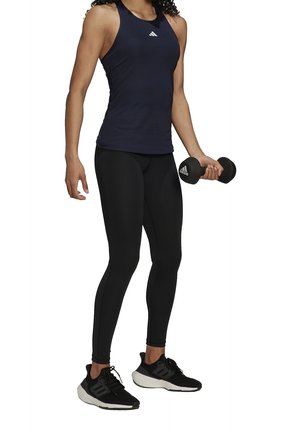 Zwarte sportleggings en een marineblauwe tanktop. De persoon houdt een zwarte dumbbell vast en draagt zwarte hardloopschoenen met witte zolen.
