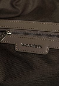 Ciemnobrązowa torba z tkaniny z szarym zamknięciem na zamek błyskawiczny oraz teksturowanym skórzanym naszywką z wytłoczonym słowem "wonders."