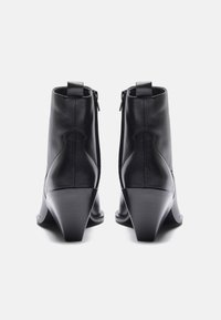 Bottines en cuir noir avec un talon compensé et une pointe effilée. Présentent une fermeture éclair à l'arrière et une texture lisse.