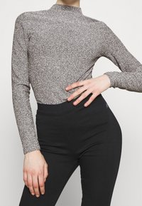 Glittery silver long-sleeve top with a high mock neck, paired with high-waisted black pants; sleek, fitted silhouette.