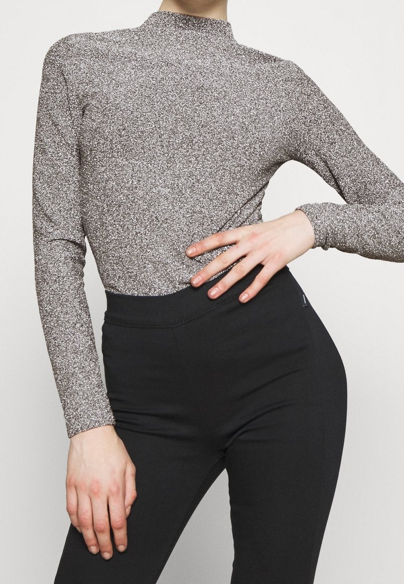 Glittery silver long-sleeve top with a high mock neck, paired with high-waisted black pants; sleek, fitted silhouette.