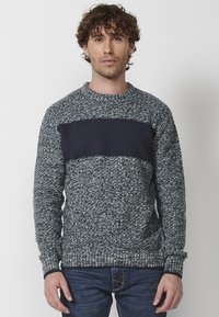 Suéter de punto con un cuerpo texturizado en gris-azul y un panel sólido en azul marino en el pecho. Puños y dobladillo acanalados.