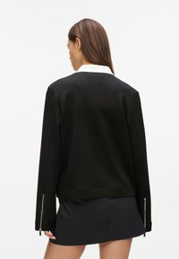 Čierna mikina s bielym golierom, dlhými rukávmi a striebornými detailmi na manžetách. Jednoduchý, minimalistický dizajn.