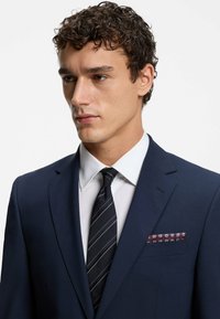Giacca da abito blu navy con revers a notched, camicia bianca e cravatta a righe. Presenta un fazzoletto da taschino decorato in tonalità di bordeaux e blu.