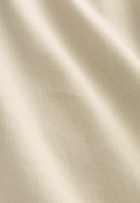 Világos bézs szövet, sima textúrával, finom bordázattal és lágy fényességgel, elegánsan hullámzó puha redőkben. 