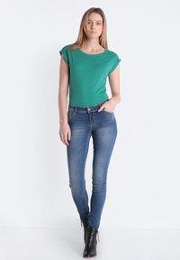 Top verde de manga corta con escote redondeado, combinado con unos jeans de denim azules ajustados. El look se completa con botas de tacón negro hasta el tobillo.