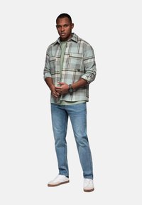 Camisa de cuadros verde claro sobre una camiseta gris, combinada con jeans azul claro y zapatillas blancas con detalles marrones.
