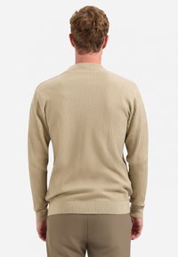 Beige geribbelde trui met een ronde hals, lange mouwen en een aansluitende tailleband, gemaakt van een gestructureerd breimateriaal.