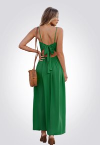 Robe maxi verte avec un détail noué dans le dos, des bretelles fines et une silhouette fluide. Assortie à un sac en bandoulière tissé et des chaussures à talons.