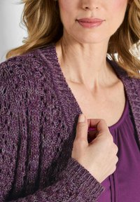 Cardigan viola lavorato a maglia con un motivo testurizzato a punto aperto, dotato di colletto e polsini a costine, indossato sopra una maglietta viola.