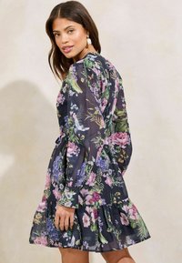 Bloemenjurk met een donker marineblauwe achtergrond, versierd met levendige roze en paarse bloemen, lange mouwen, een gerimpelde zoom en een losse pasvorm.