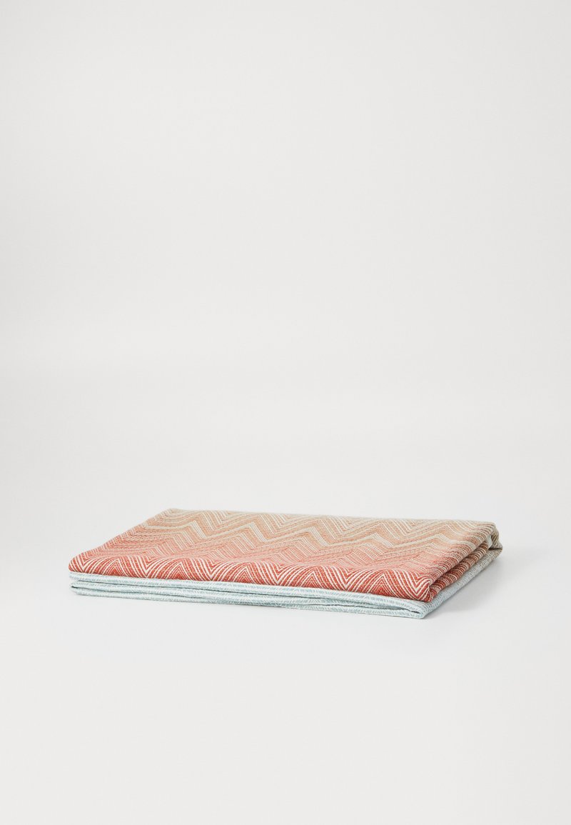 Složená deka s texturovaným vzorem chevron v odstínech červené a krémové, překrytá světle modrou tkaninou, s čistými okraji.