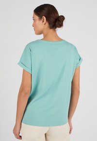 Camiseta verde menta con mangas enrolladas y un corte relajado, con un cuello redondo y material de algodón suave. Sin estampados ni patrones visibles.
