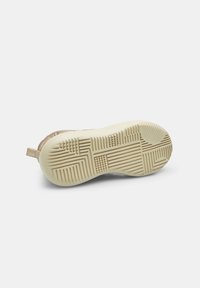 Suela de sneaker beige con goma texturizada para agarre, que presenta un patrón sutil con líneas levantadas. Tacón plano y pequeño lazo trasero para facilitar el uso.