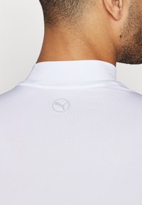 Valge sportlik polo-särk kõrge kraega. Omab tekstuuriga kangast ning seljal on ümmargune hall logo. Puhtad ja minimalistlikud jooned.