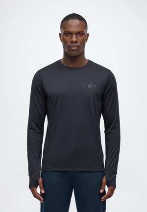 Homme debout face à l'avant portant un maillot de sport noir ajusté à manches longues avec le logo "Ted Baker Sport" sur la poitrine gauche.