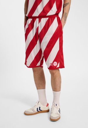 Mand iført røde og hvide stribede sportsshorts og matchende top, hvide sokker og hvide sneakers med blå og røde detaljer.