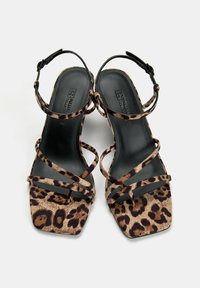 Sandales à talons hauts en imprimé léopard avec un embout carré, plusieurs brides croisées et une semelle intérieure en cuir noir. Sangle de cheville ajustable incluse.