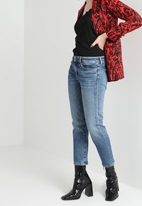 Red and black patterned blazer over a black top, paired with light blue denim jeans and shiny black ankle boots with a block heel.