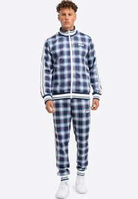 Marineblauw geruit trainingspak met rode en witte accenten. Op-en-top jack en bijpassende broek, beide met gestreepte manchetten en tailleband.
