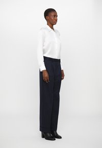White button-up shirt with long sleeves, paired with navy pinstripe trousers. Trousers feature a relaxed fit and are slightly cropped at the ankle.