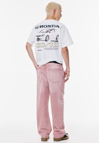 Witte grafische t-shirt met een Honda Civic ontwerp op de achterkant, gecombineerd met losse rozenkleuren spijkerbroek en platform schoenen.
