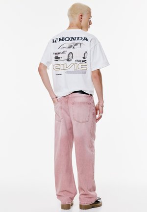 Weißes Grafik-T-Shirt mit einem Honda Civic Design auf dem Rücken, kombiniert mit lockeren rosa Jeans und Plateausohlen.
