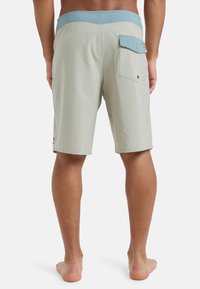 Svetlo šedé plavky s modrým pásom, so zadnou vreckom a hladkou textúrou. Navrhnuté pre pohodlie a pohyblivosť.