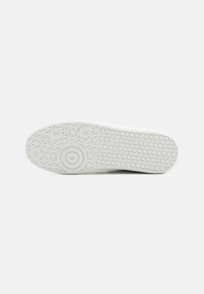 Suola di sneaker bianca con una presa in gomma testurizzata, caratterizzata da motivi circolari e un disegno a diamante per garantire aderenza.